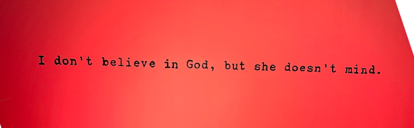 Shows black text on pink background: 'I don't believe in God, but she doesn't mind.'